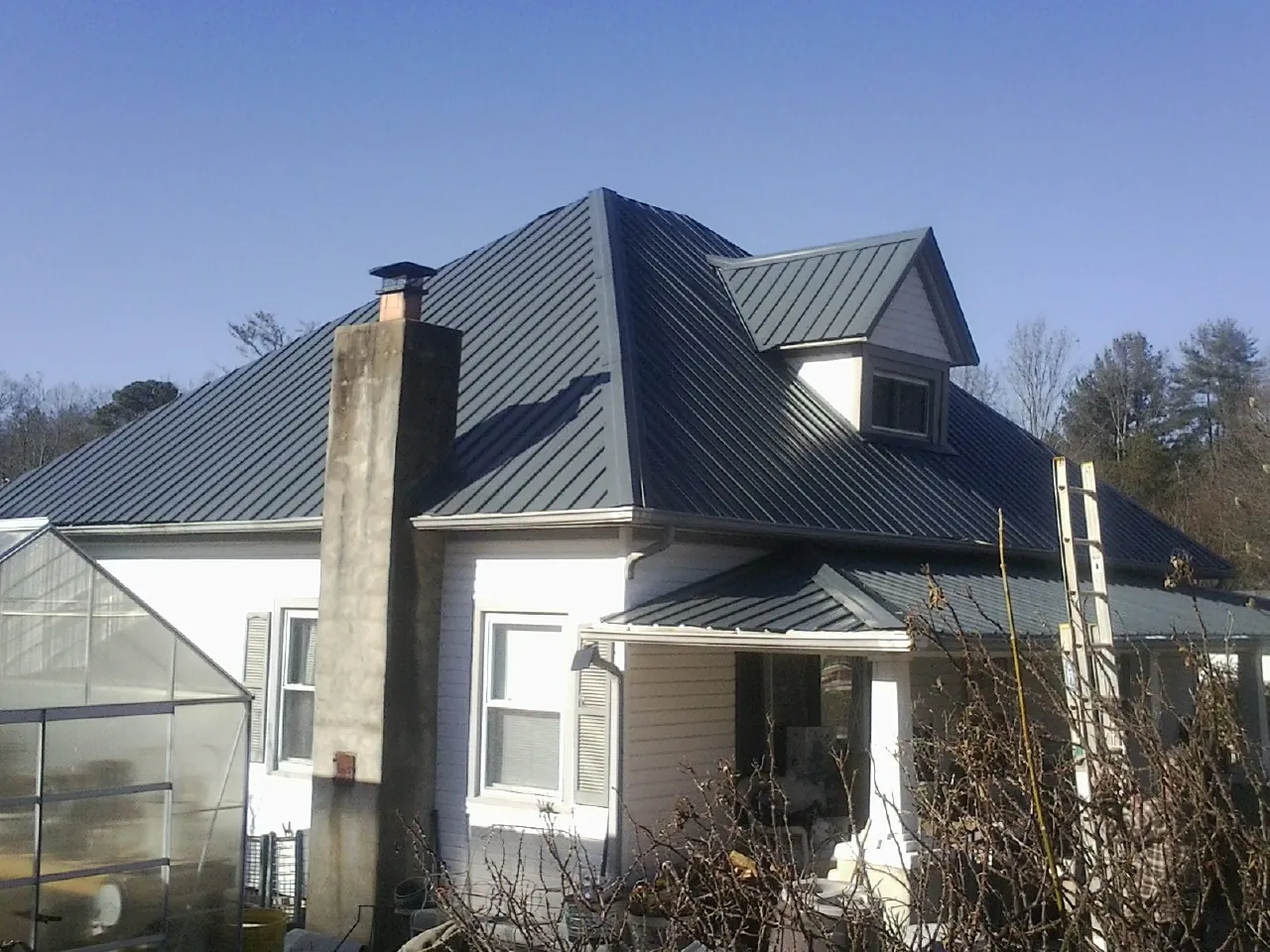 Dark blue standing seam metal roof on a white farmhouse with dormer — Slate & Tile Roof Repair by Roofing Brothers in East Granby