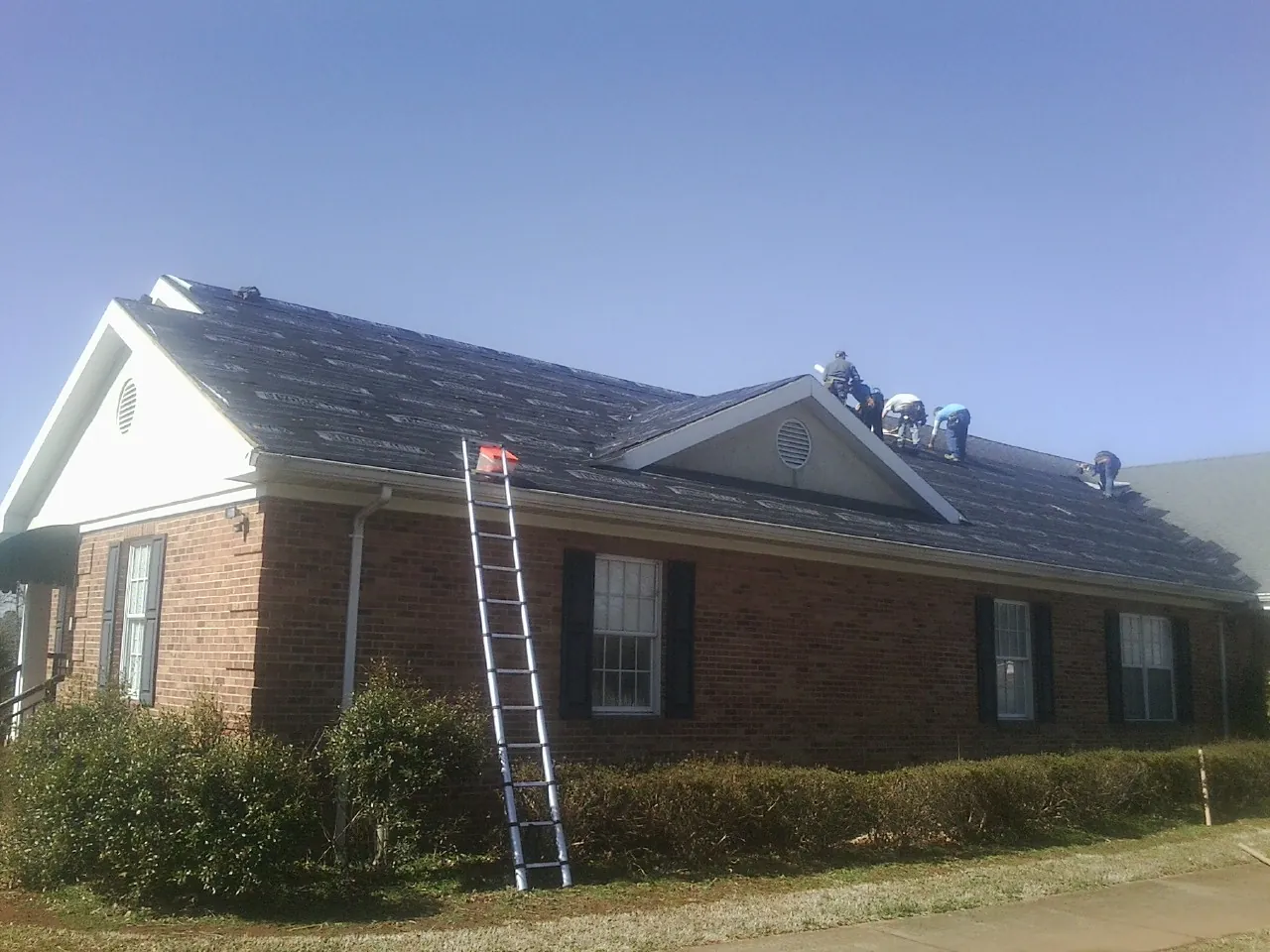 Crew tearing shingles off a brick ranch roof with a ladder set — Metal Roof Repair work by our crew in East Granby
