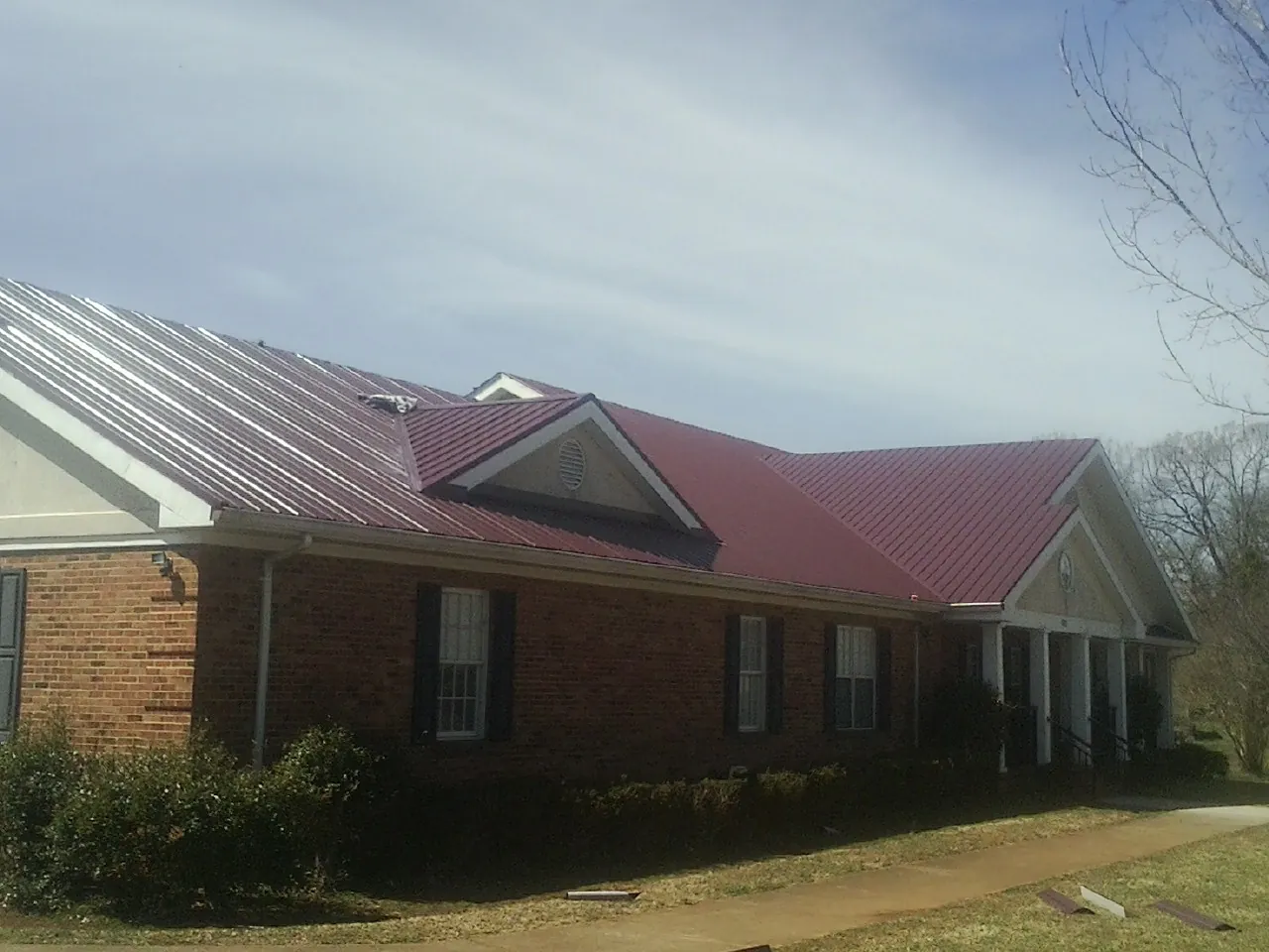 Red metal roof with gabled entries on a long brick building, from a Hail Damage Roof Repair job in East Granby
