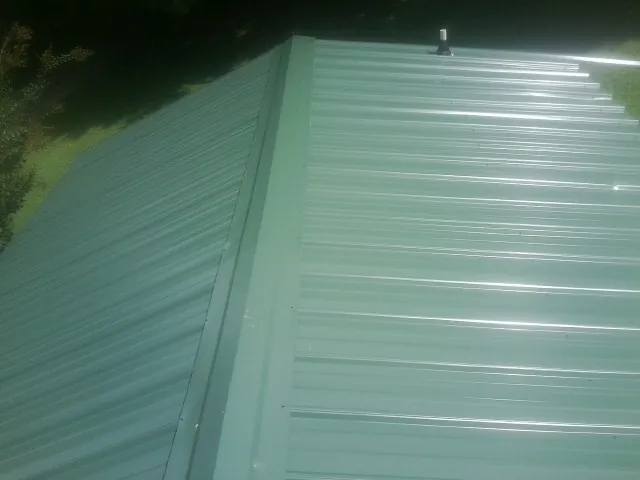New green metal panels meeting at the ridge of a roof — Flat Roof Repair work by our crew in East Granby