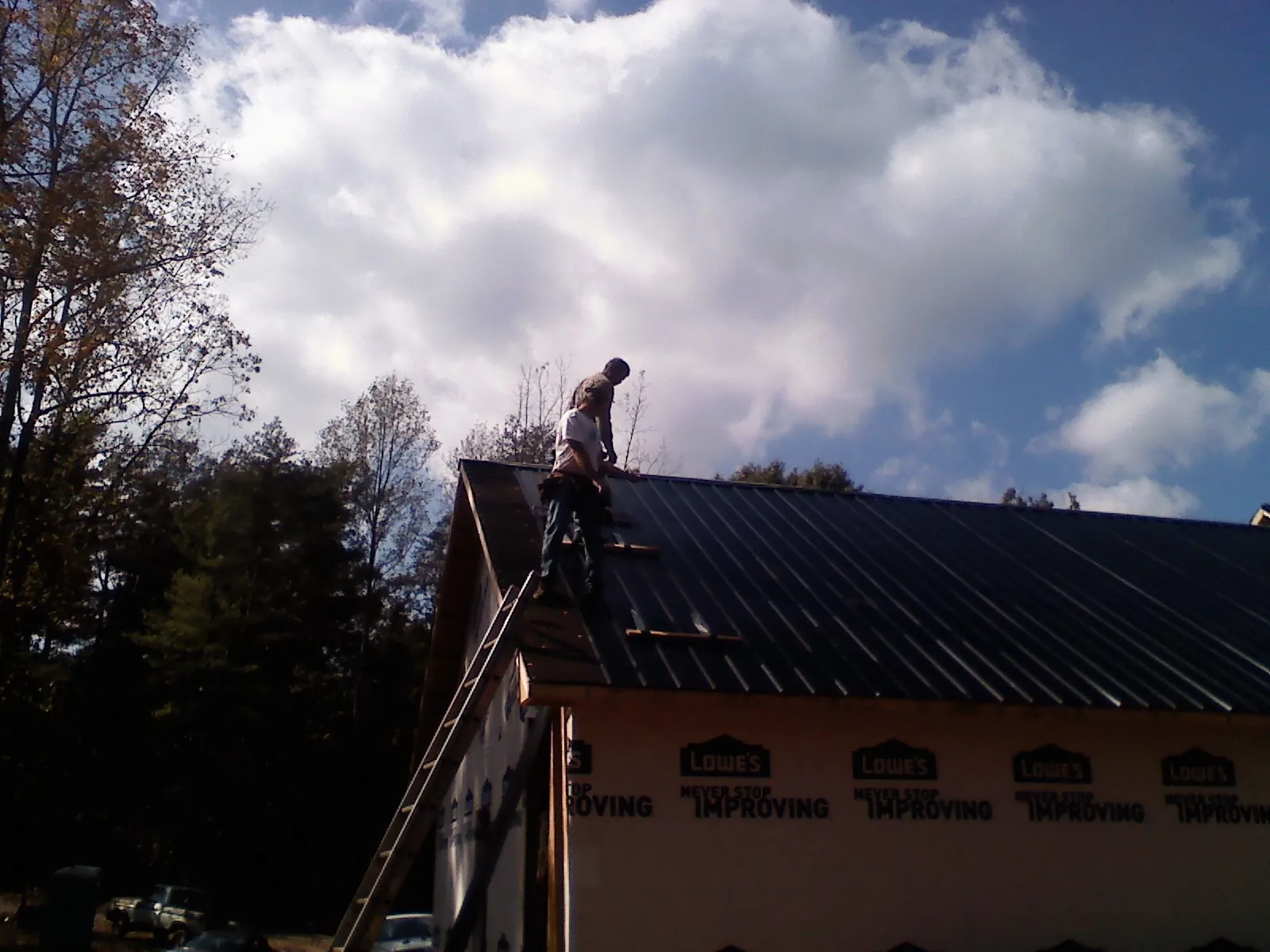 Roofer fastening dark metal panels high against a cloudy sky, from a Roof Inspection job in East Granby
