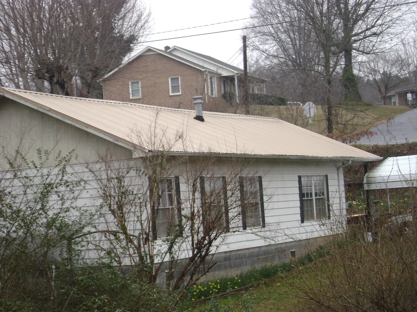 Tan metal roof on a white sided house set into a hillside — Commercial Roofing by Roofing Brothers in East Granby